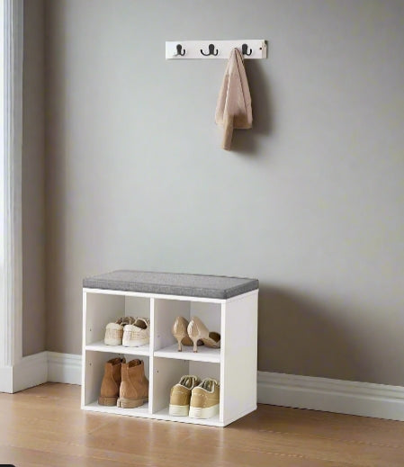 White shoe storage bench with gray cushioned top against a gray wall with hooks.