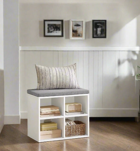 White storage bench with a cushion in a room with framed pictures on the wall.