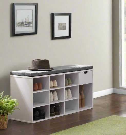 White shoe storage bench with gray top in a room with framed pictures on the wall.