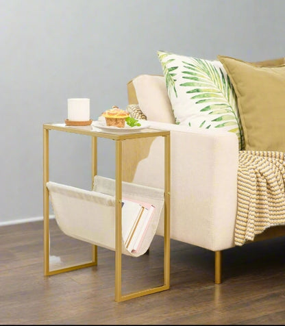 Slim gold side table with clear glass top and linen fabric magazine rack, perfect for small spaces like bedrooms or narrow living room corners

